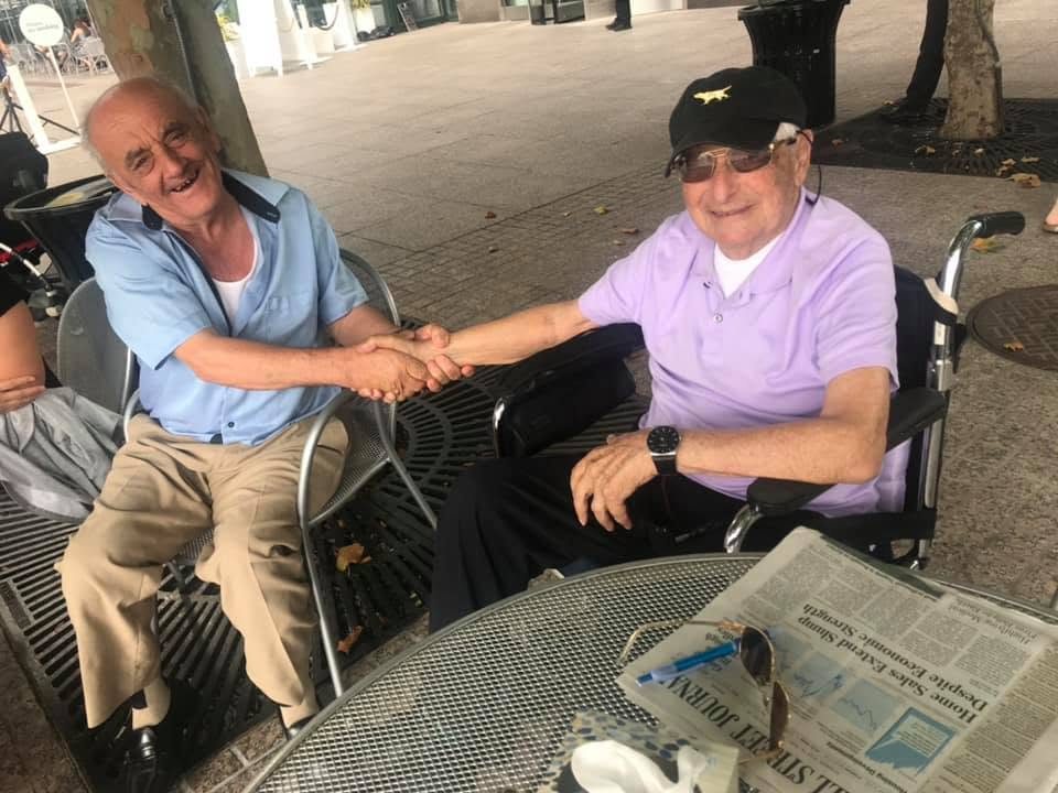 Two clients laughing and shaking hands at an outdoor cafe table