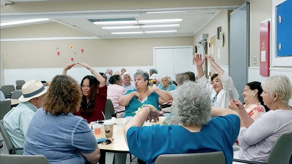 A busy community activity room with seniors seated at tables