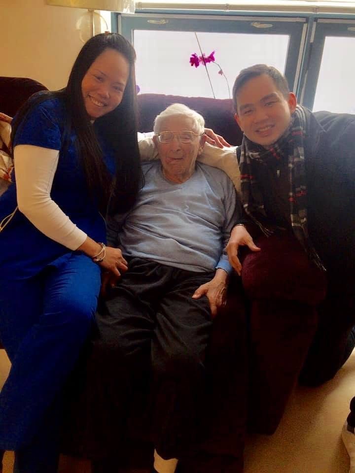 Two caregivers seated either side of a client in his own living room